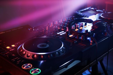Closeup view of modern DJ controller with headphones on color background