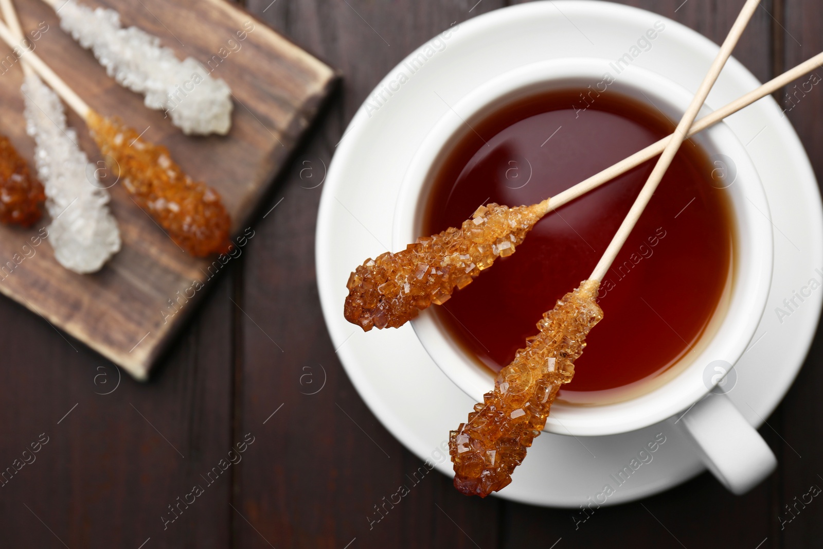 Photo of Sticks with sugar crystals served to tea on wooden table, flat lay
