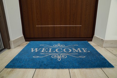 Photo of Beautiful blue doormat with word Welcome on floor near entrance