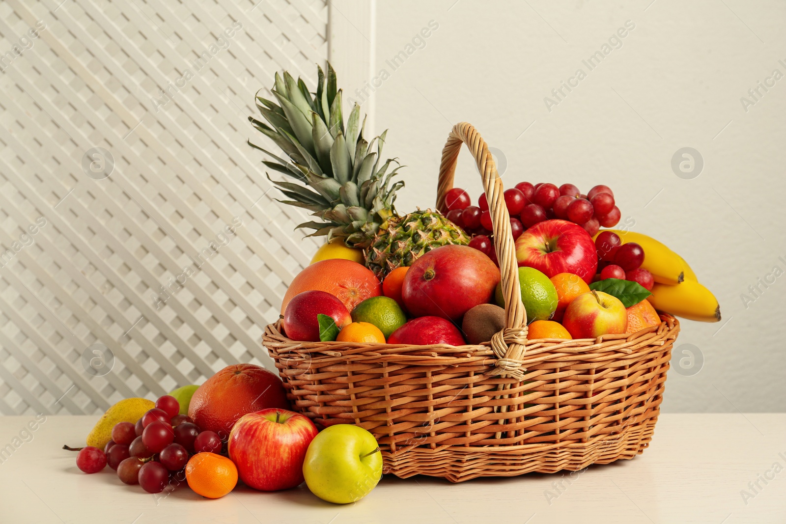 Photo of Wicker basket with different fresh fruits on white wooden table