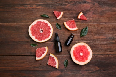 Flat lay composition with grapefruit slices and bottles of essential oil on wooden background