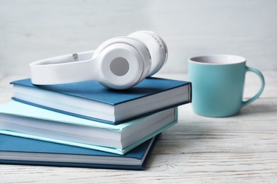 Photo of Modern headphones with hardcover books on wooden table. Space for text