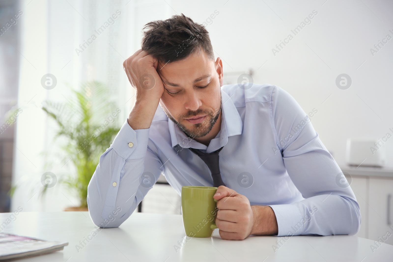 Photo of Sleepy man with cup of drink at home in morning