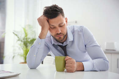 Photo of Sleepy man with cup of drink at home in morning