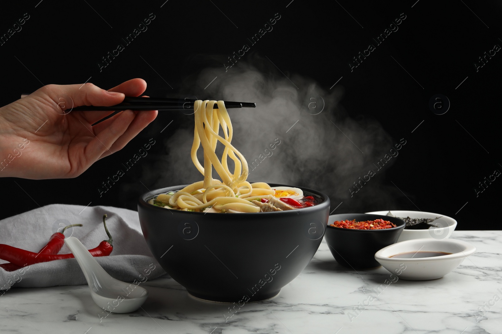 Photo of Woman eating delicious ramen with chopsticks at white marble table, closeup. Noodle soup