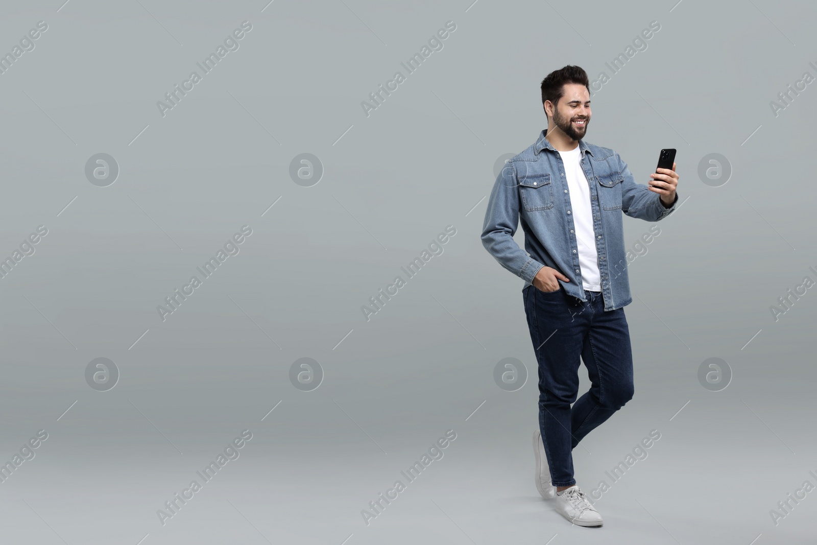 Photo of Happy young man using smartphone on grey background, space for text