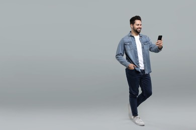 Happy young man using smartphone on grey background, space for text