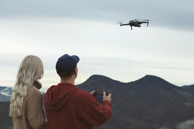 Young couple operating modern drone with remote control in mountains, back view