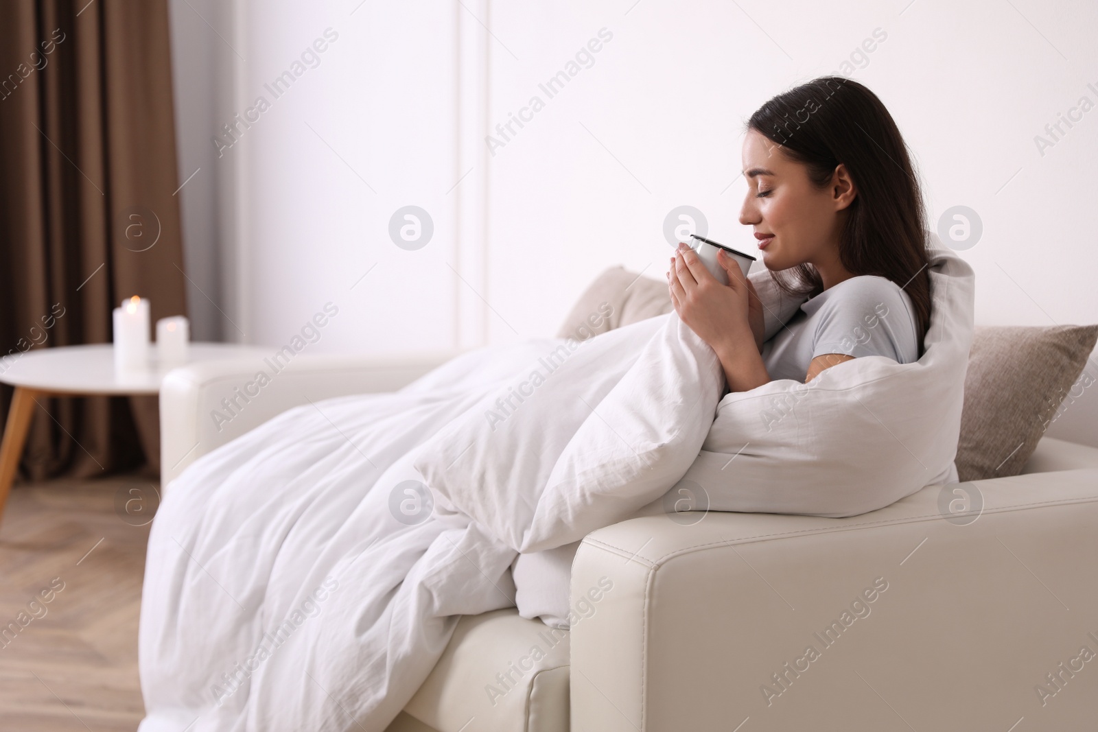 Photo of Woman covered in blanket holding cup of drink on sofa, space for text