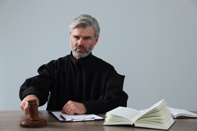 Photo of Judge with gavel, papers and book sitting at wooden table against light grey background
