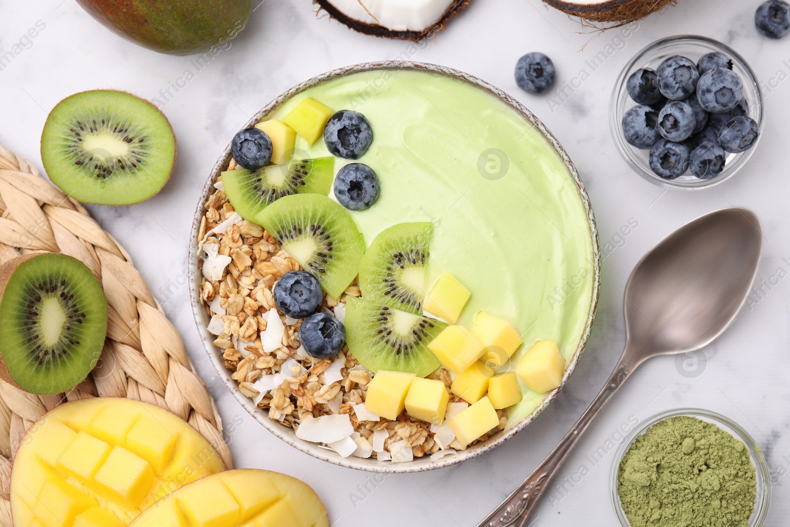 Photo of Tasty matcha smoothie bowl with fresh fruits and oatmeal served on white marble table, flat lay. Healthy breakfast