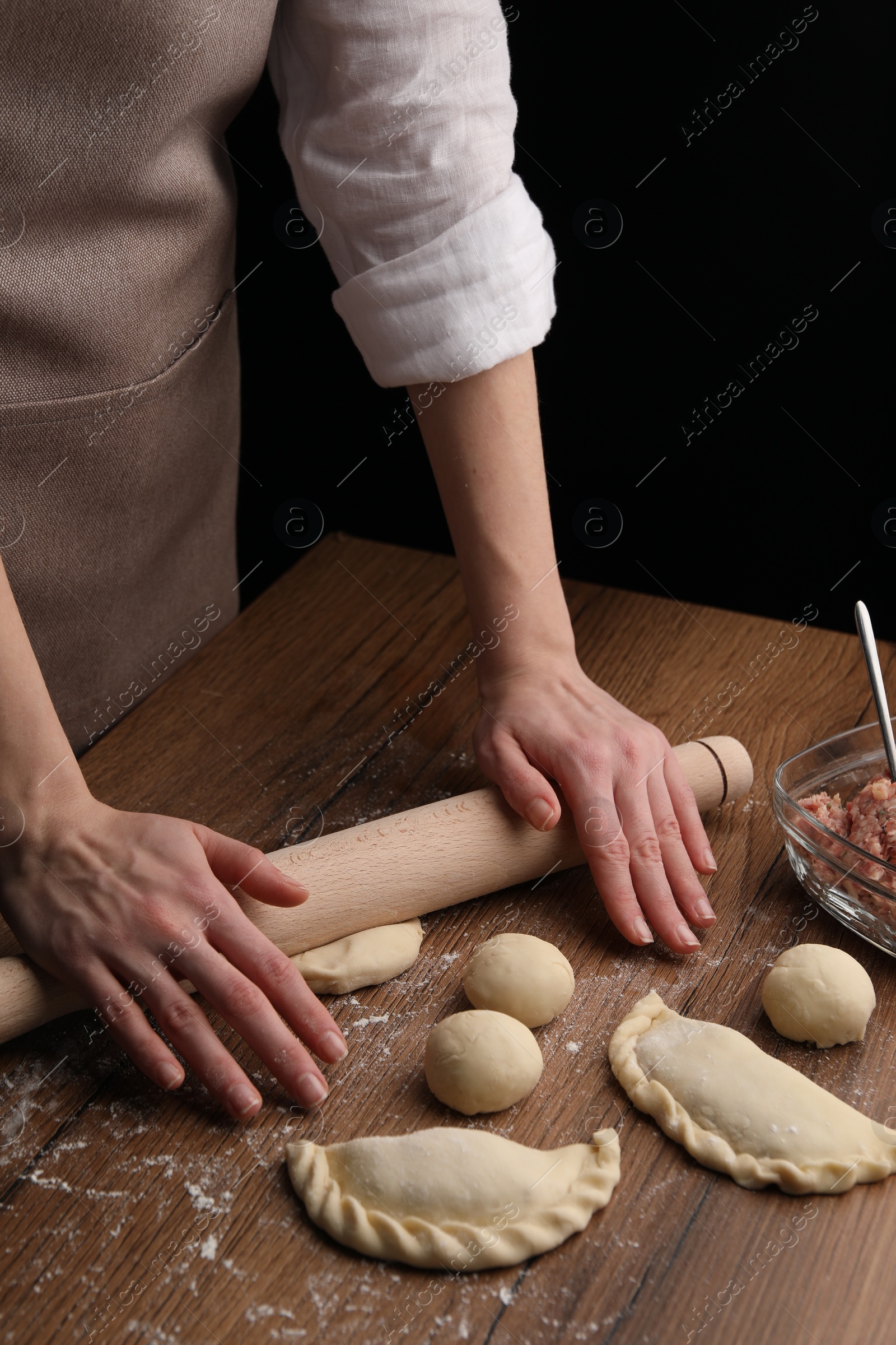 Photo of Woman rolling dough for chebureki on wooden table, closeup