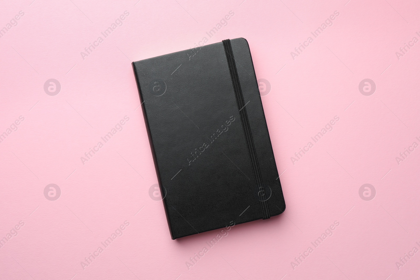 Photo of Closed black notebook on light pink background, top view