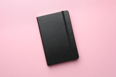 Closed black notebook on light pink background, top view