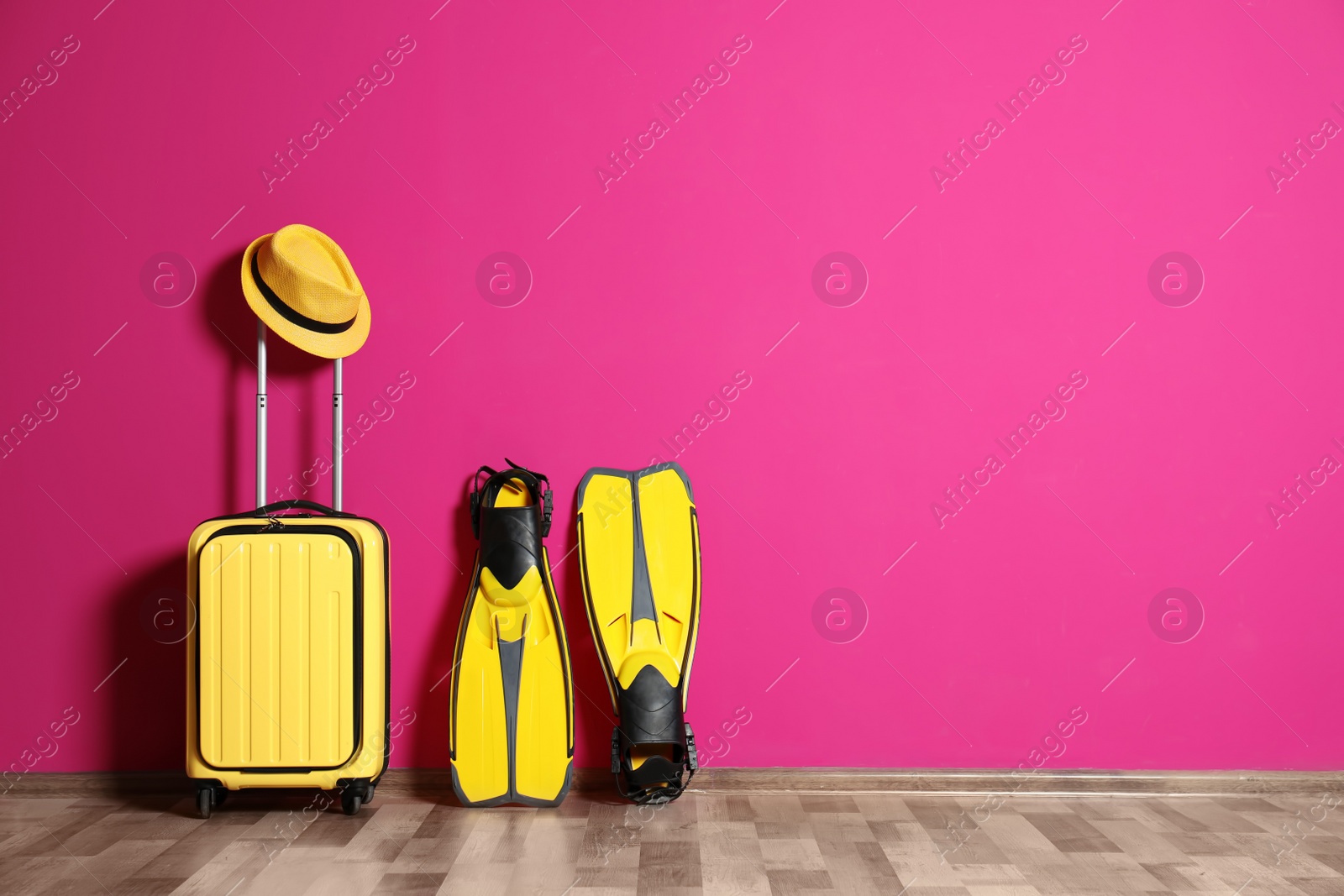 Photo of Suitcase with hat and swim fins near color wall. Space for design