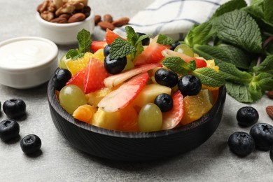 Delicious fruit salad in bowl, berries, nuts and fresh mint on grey table