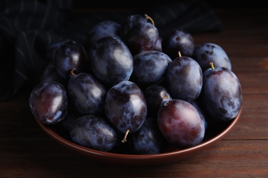 Delicious ripe plums in bowl on wooden table