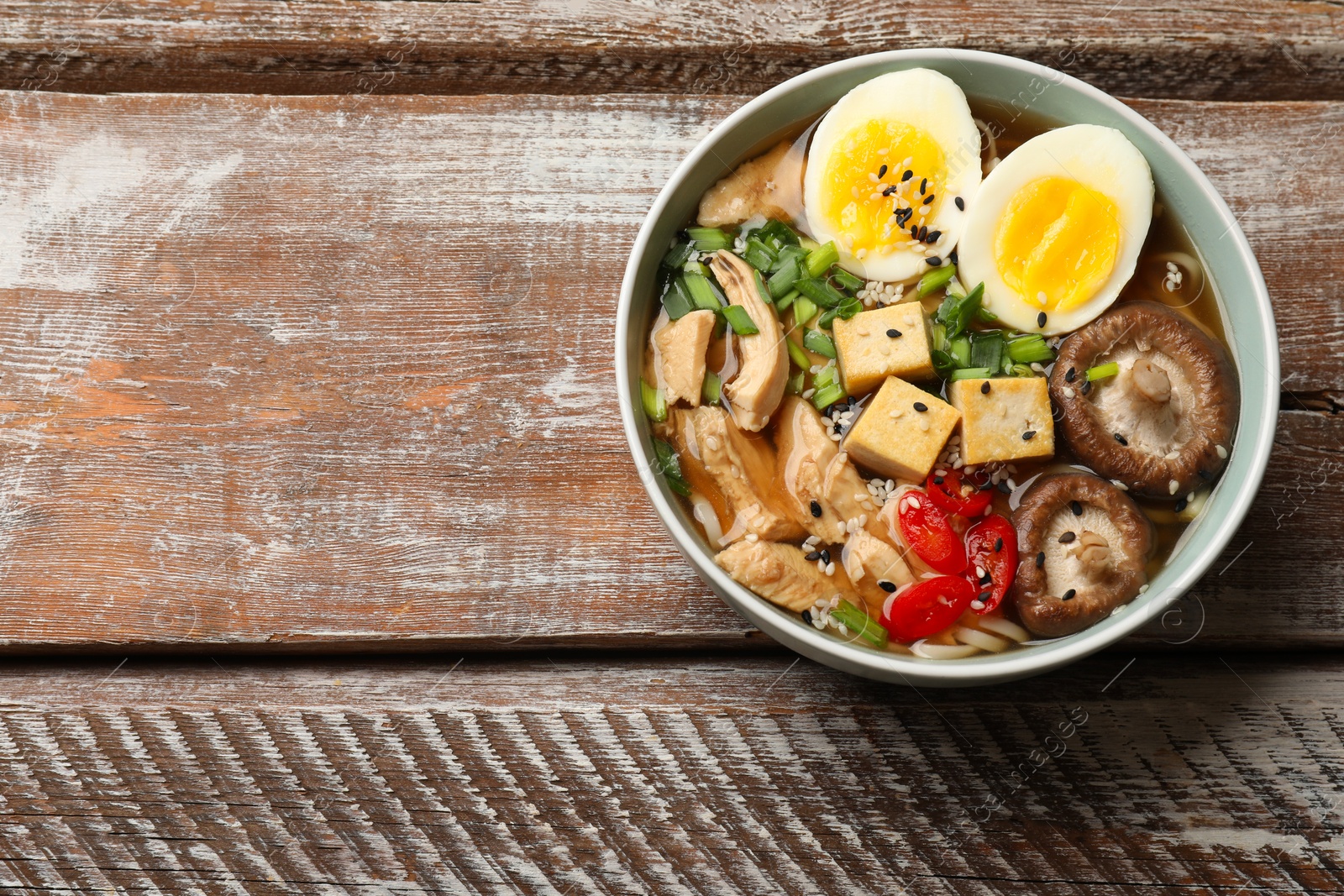 Photo of Bowl of delicious ramen on wooden table, top view with space for text. Noodle soup