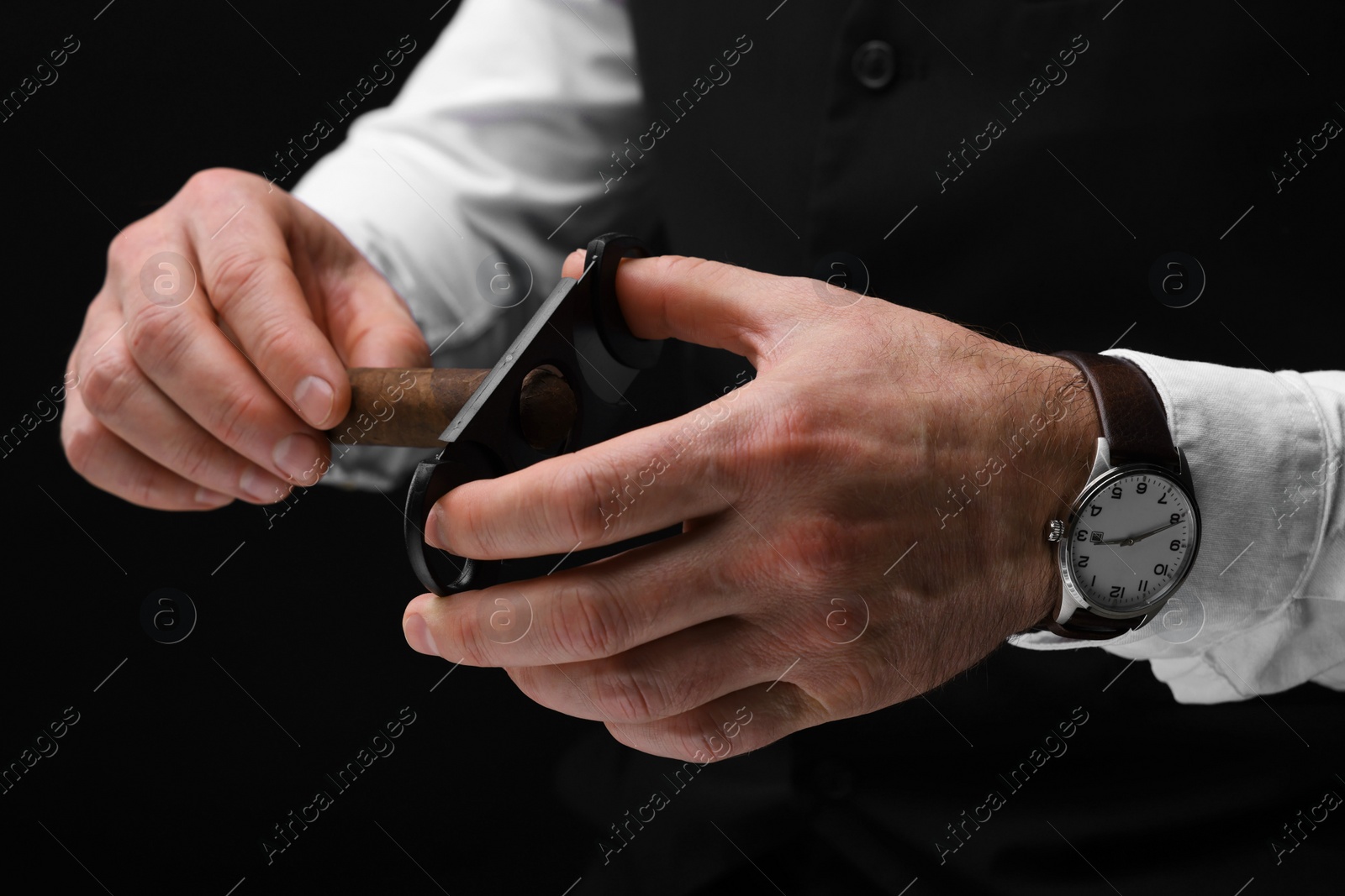 Photo of Man cutting tip of cigar on black background, closeup