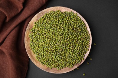 Photo of Wooden bowl with green mung beans and napkin on black background, flat lay