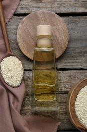 Bottle of organic sesame oil and seeds on wooden table, flat lay