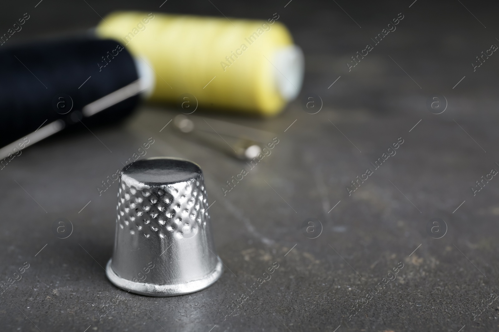 Photo of Silver sewing thimble on grey table, closeup. Space for text