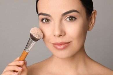 Photo of Beautiful young woman applying face powder with brush on grey background, closeup