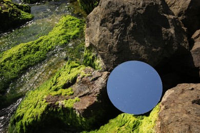 Photo of Round mirror reflecting light blue sky on stones with seaweed outdoors