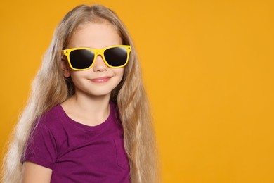 Girl wearing stylish sunglasses on orange background, space for text