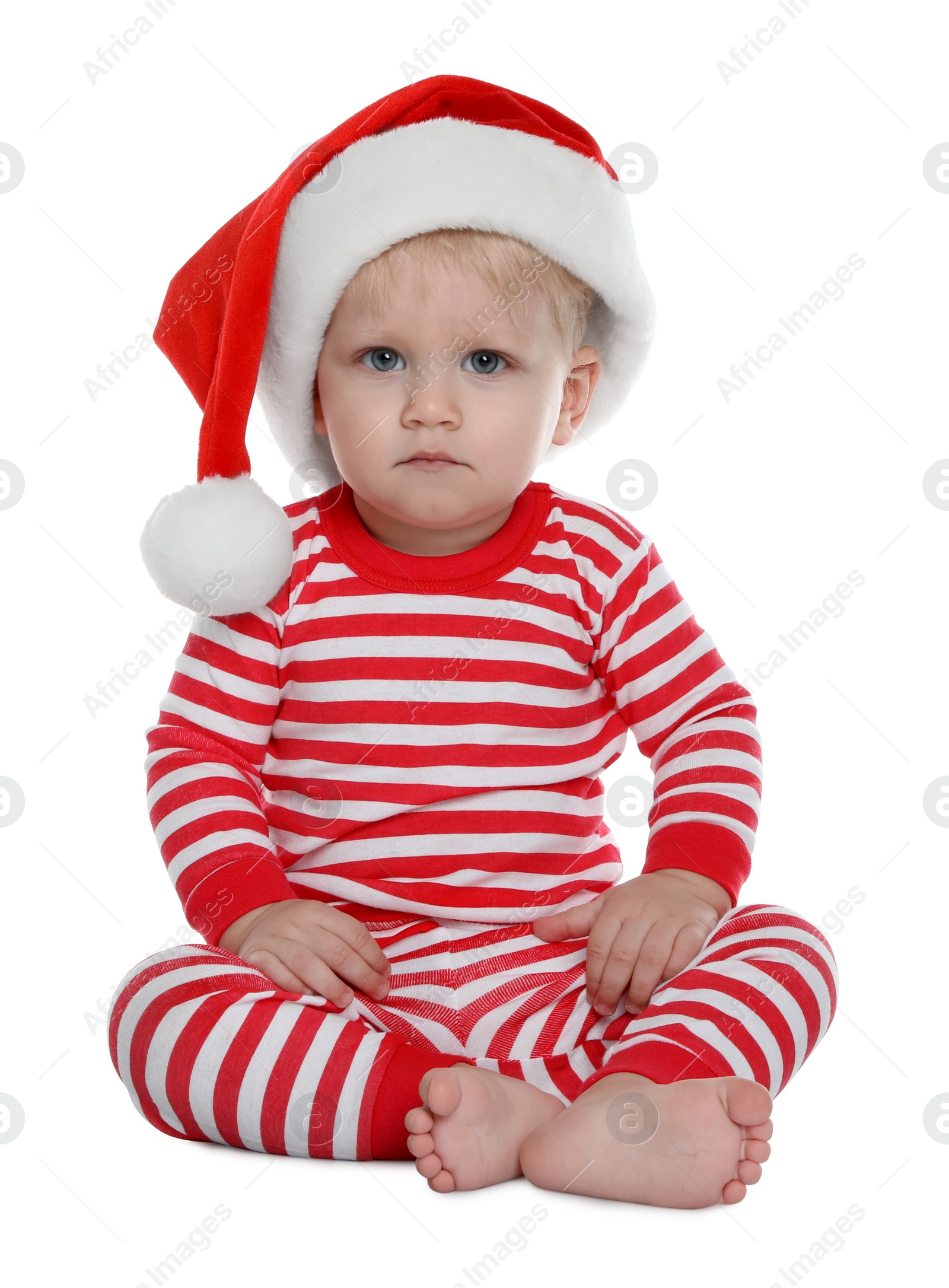 Photo of Cute baby in Santa hat and Christmas pajamas sitting on white background