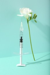 Photo of Cosmetology. Medical syringe and freesia flower on turquoise background