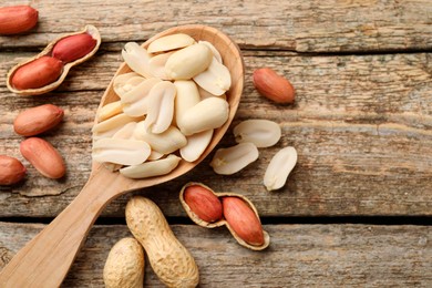 Photo of Fresh peanuts and spoon on wooden table, top view. Space for text