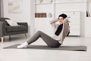 Photo of Muslim woman in hijab doing abs exercise on fitness mat at home