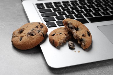 Photo of Chocolate chip cookies and laptop on light grey table, closeup