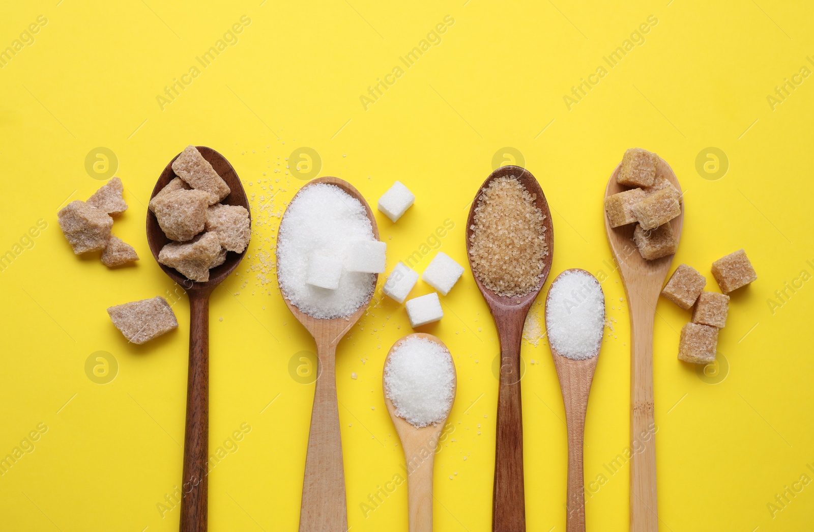 Photo of Spoons with different types of sugar on yellow background, flat lay