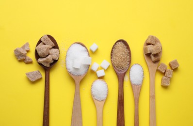Photo of Spoons with different types of sugar on yellow background, flat lay