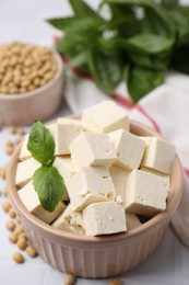 Photo of Delicious tofu cheese, basil and soybeans on white tiled table, closeup