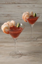 Photo of Tasty shrimp cocktail with sauce and lime in glasses on wooden table
