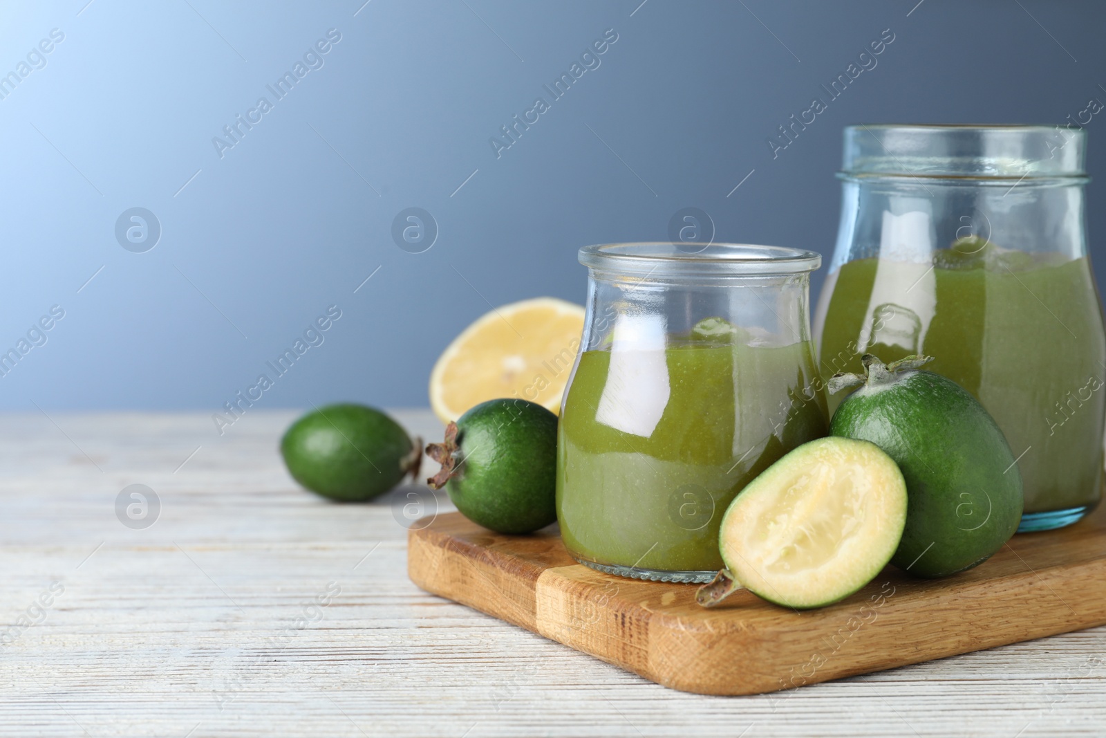 Photo of Feijoa jam and fresh fruits on white wooden table against light blue background. Space for text