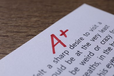 Photo of School grade. Sheet of paper with red letter A and plus symbol on wooden table, closeup
