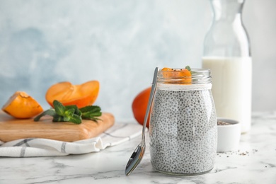 Photo of Glass jar of tasty chia seed pudding with persimmon on table. Space for text