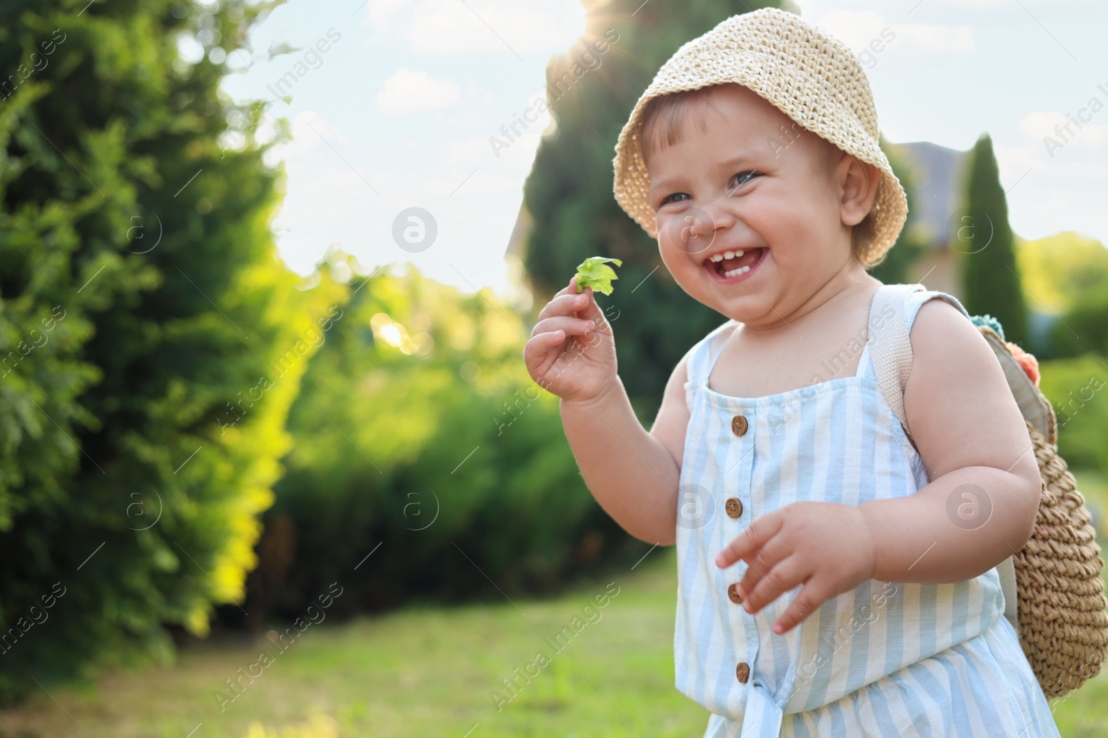 Photo of Cute little girl in stylish clothes with knitted backpack outdoors on sunny day. Space for text