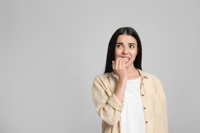 Photo of Young woman biting her nails on light grey background. Space for text