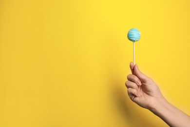 Woman holding bright delicious cake pop on color background, closeup. Space for text