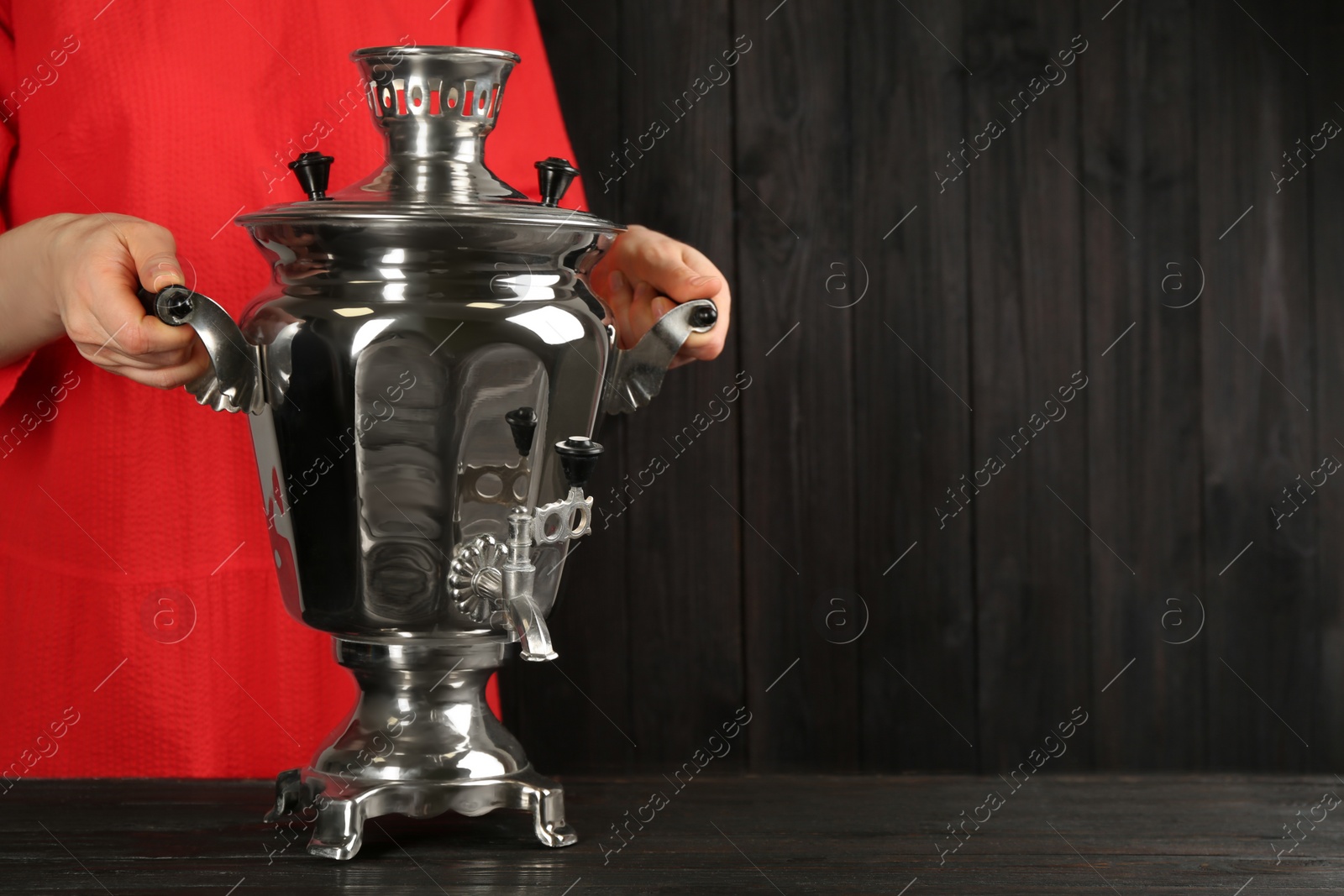 Photo of Woman holding traditional Russian samovar on dark wooden background, closeup. Space for text