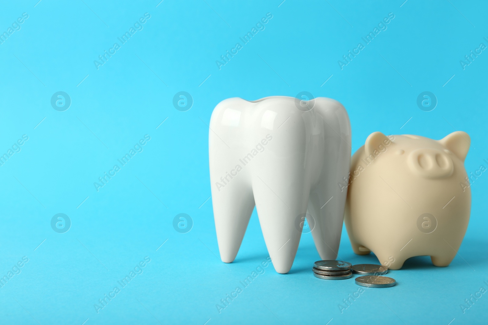 Photo of Ceramic model of tooth, piggy bank and coins on light blue background, space for text. Expensive treatment
