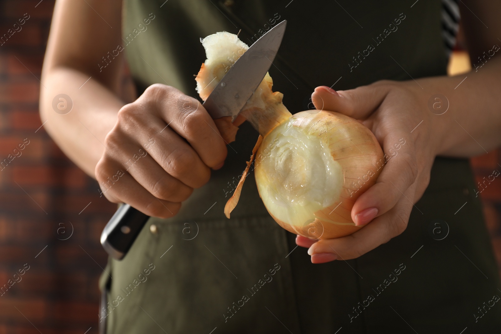 Photo of Woman peeling fresh onion with knife indoors, closeup