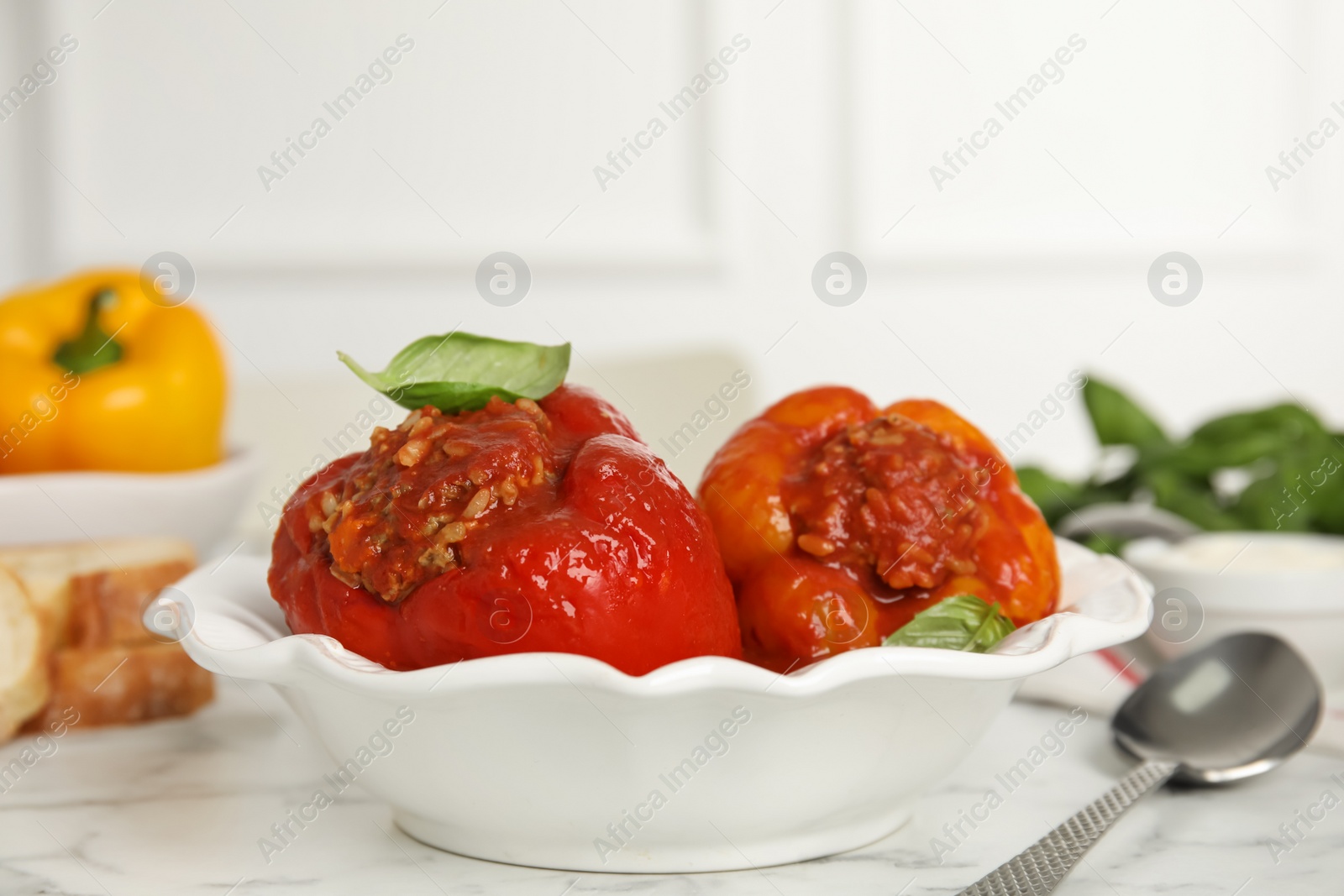 Photo of Delicious stuffed peppers with basil in bowl on white marble table