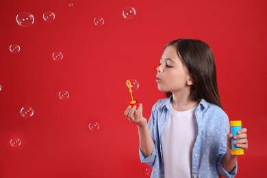 Photo of Little girl blowing soap bubbles on red background