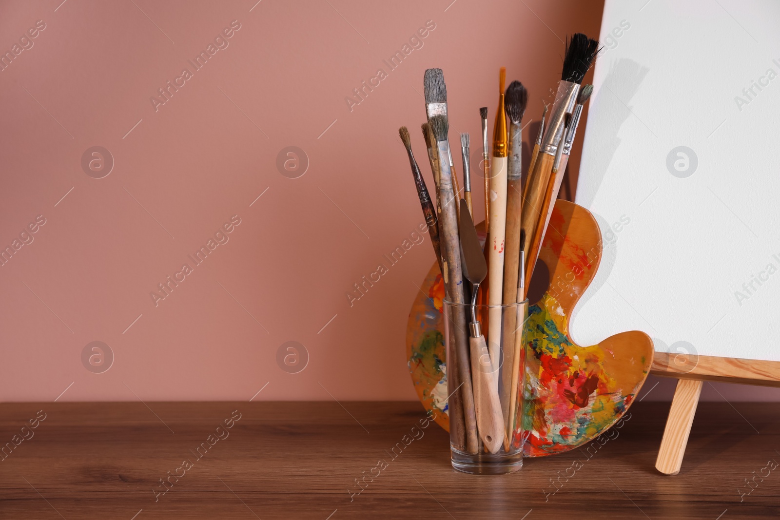 Photo of Easel with empty canvas and art supplies on wooden table. Space for text